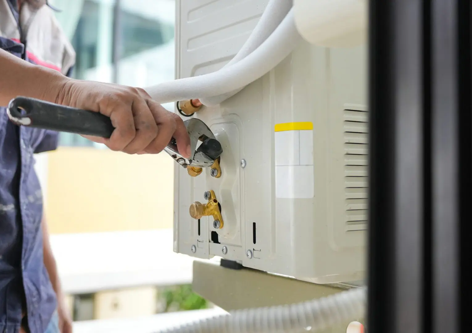 Person repairing air conditioning unit with wrench.