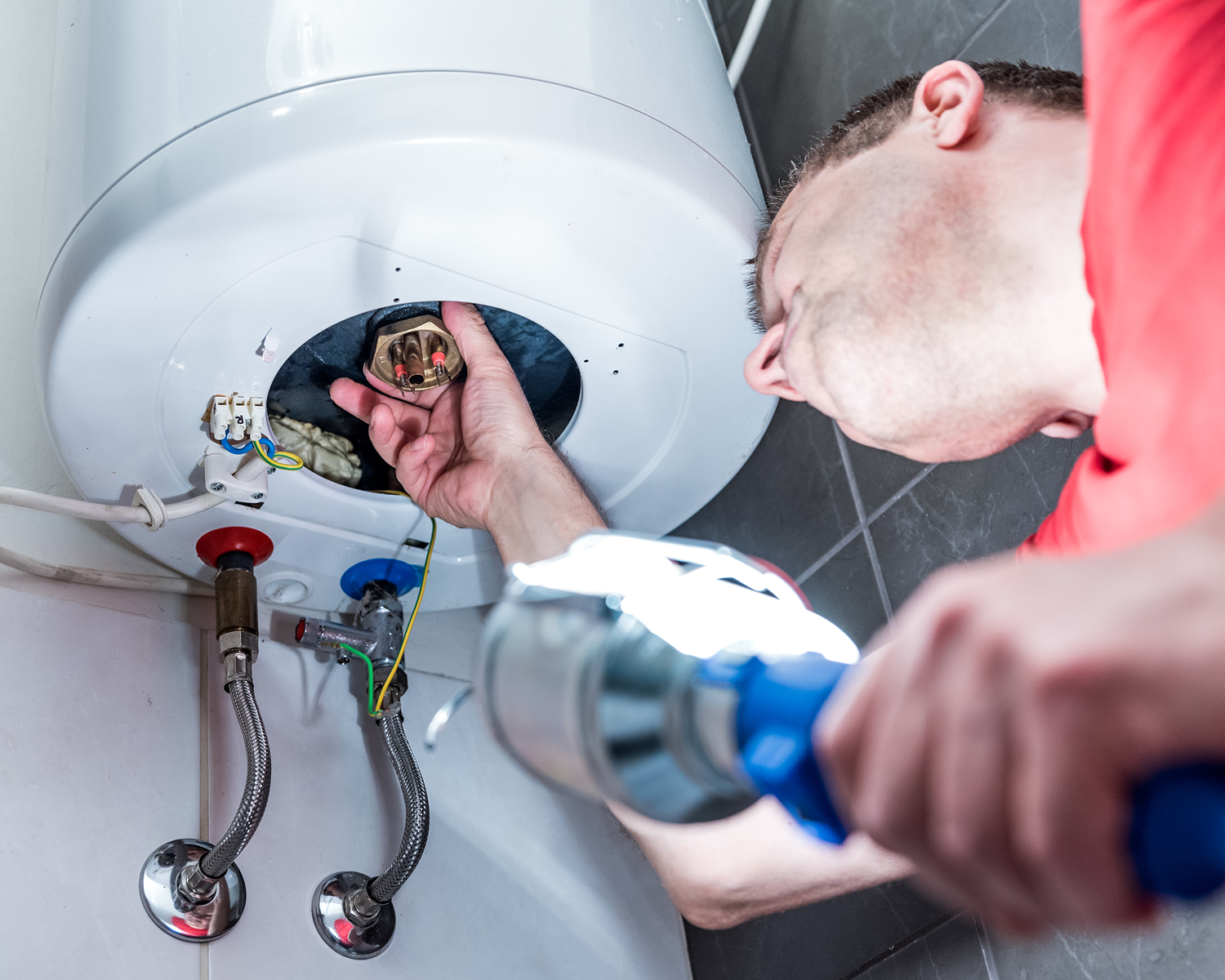 Man repairing a water heater with flashlight.