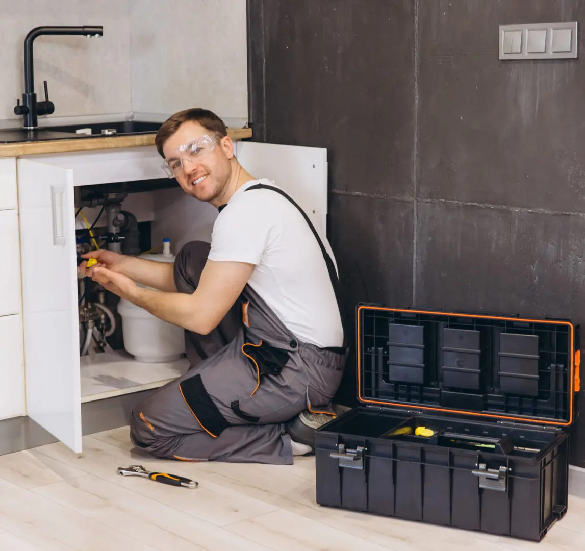 Plumber fixing sink with toolbox nearby.