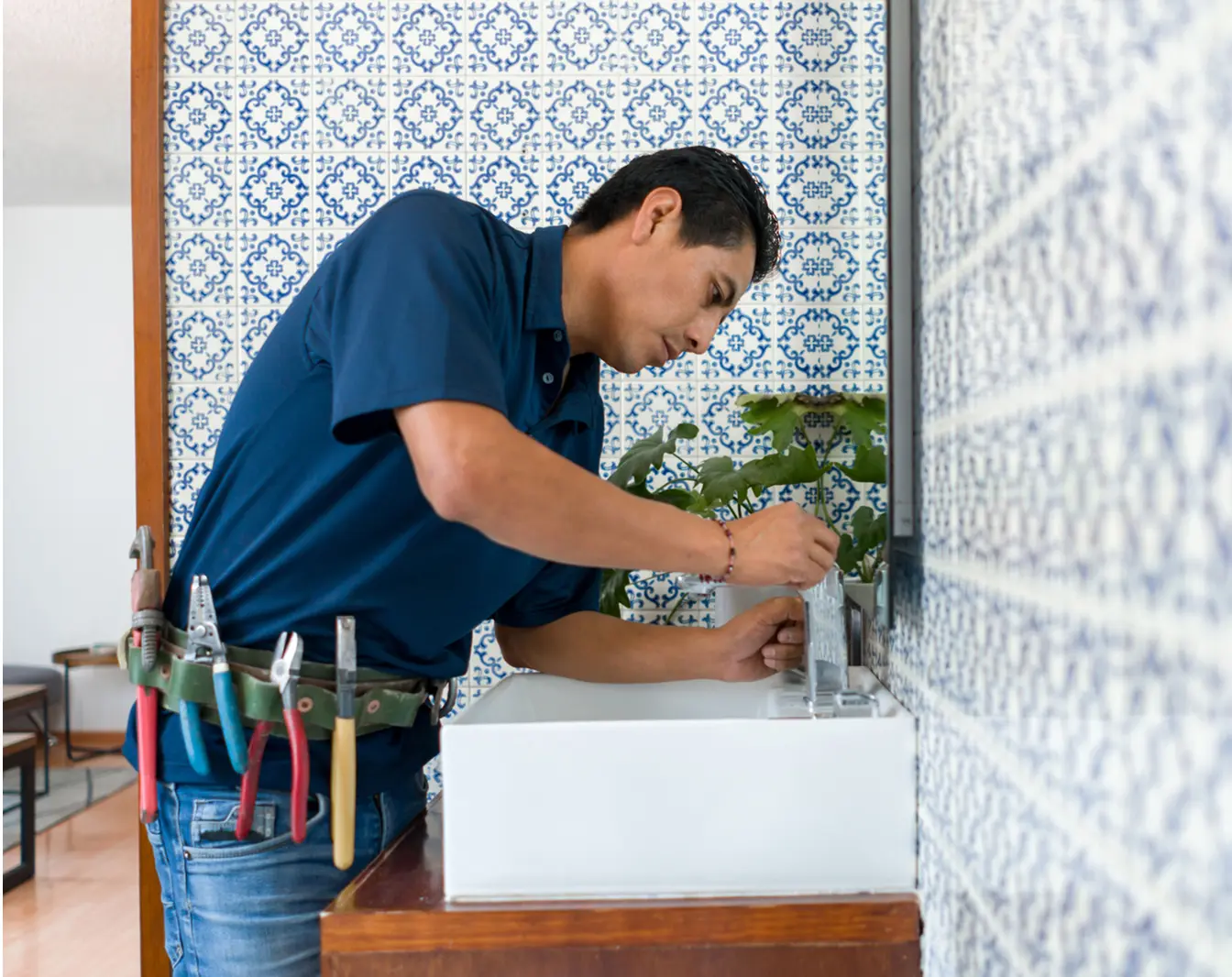 Man repairing sink in tiled bathroom.