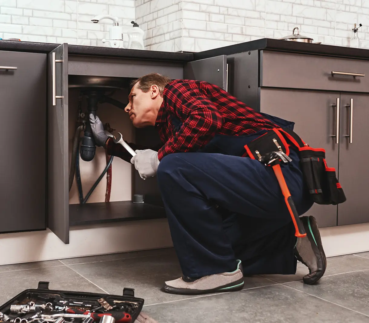 Plumber fixing kitchen sink with tools nearby.