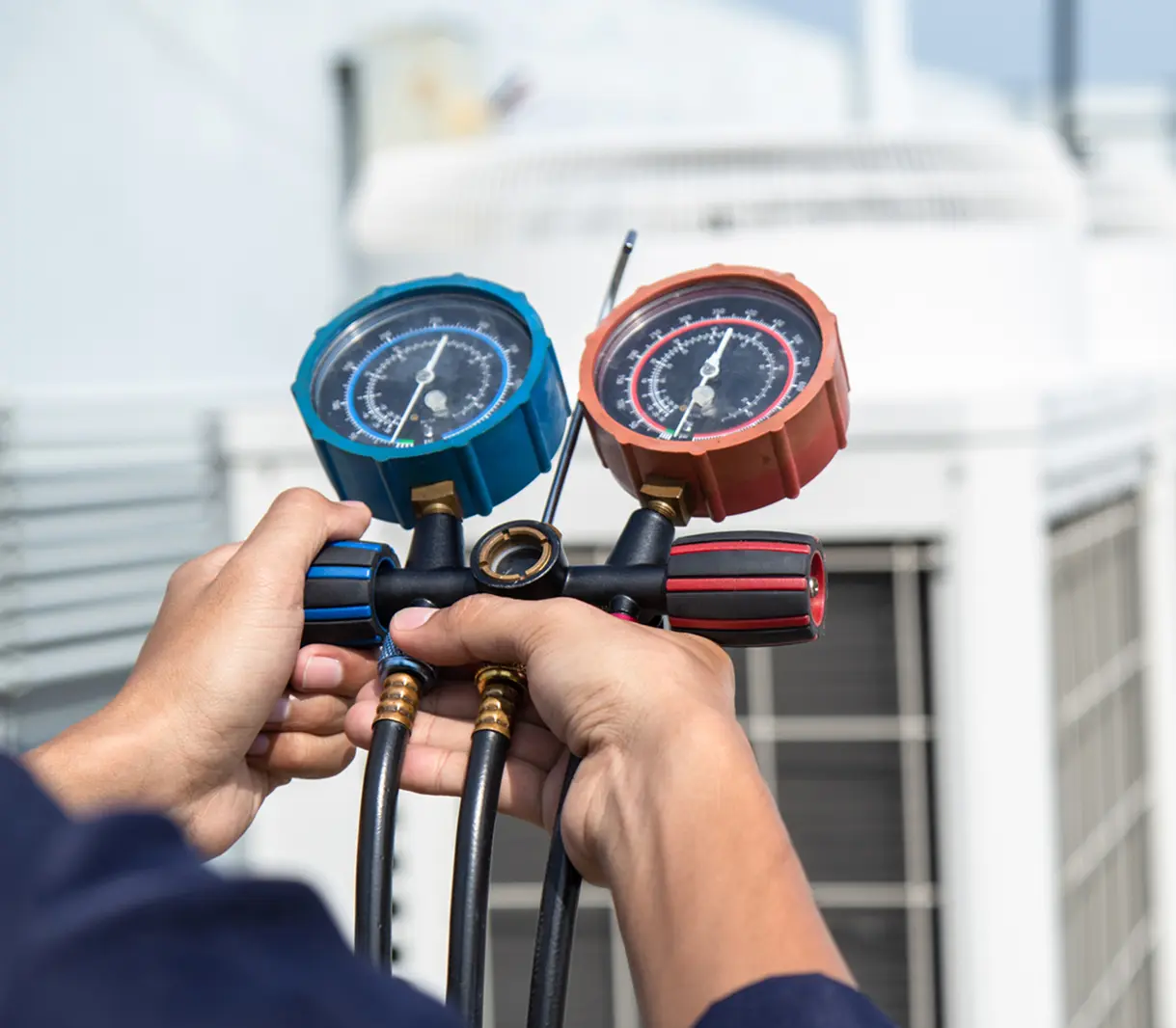 Hands holding HVAC pressure gauges near unit.