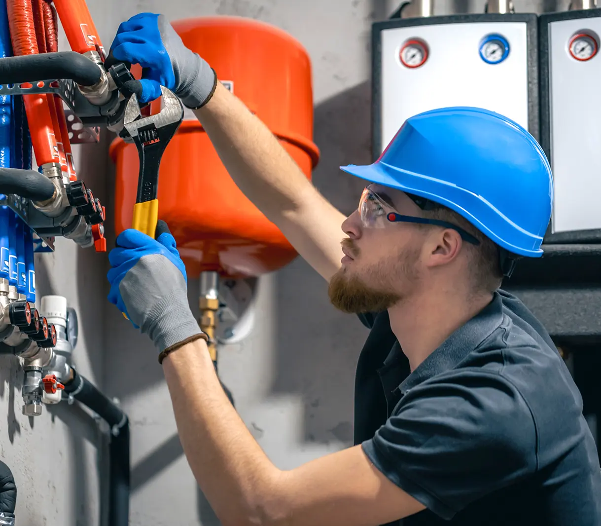 Worker adjusting pipes with wrench, wearing helmet.