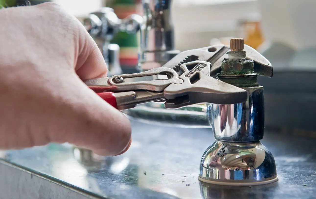 Hand using pliers to tighten sink faucet