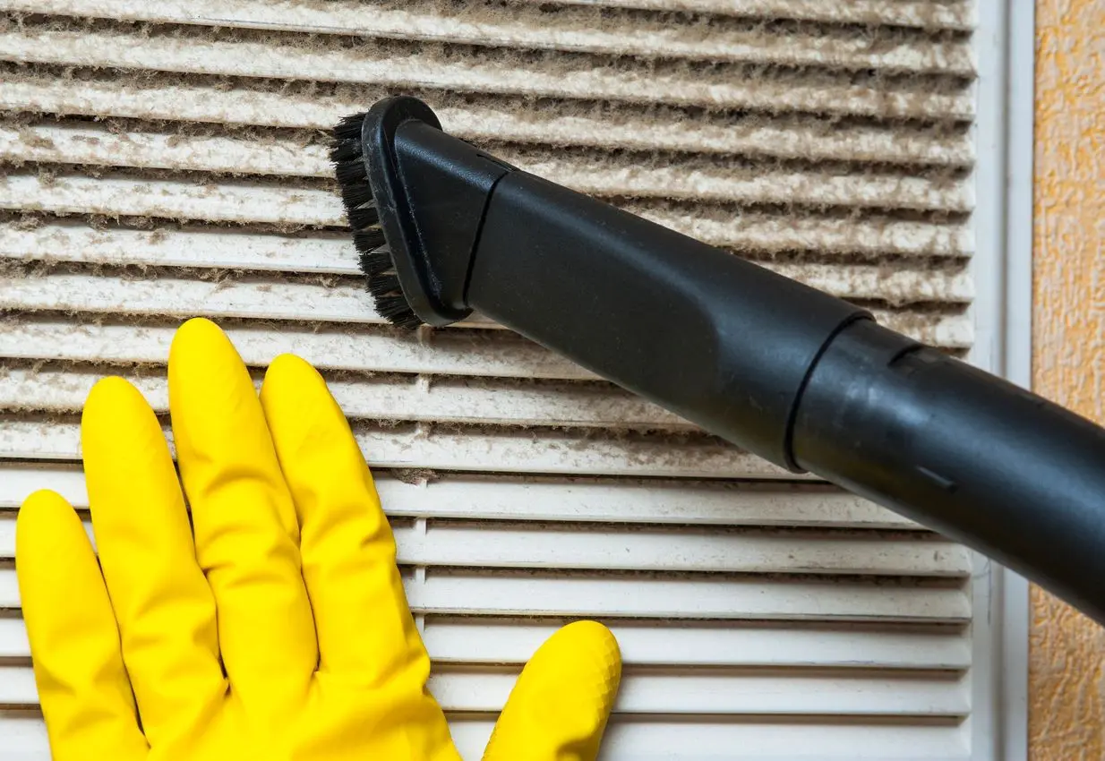 Gloved hand vacuuming dusty air vent