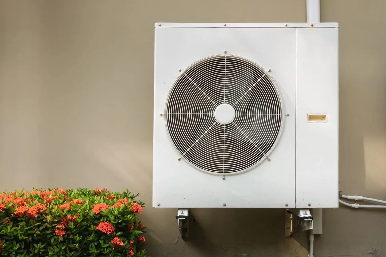 Outdoor air conditioning condenser beside flowering shrub