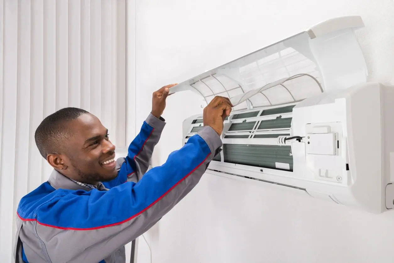 Smiling technician servicing wall-mounted air conditioner
