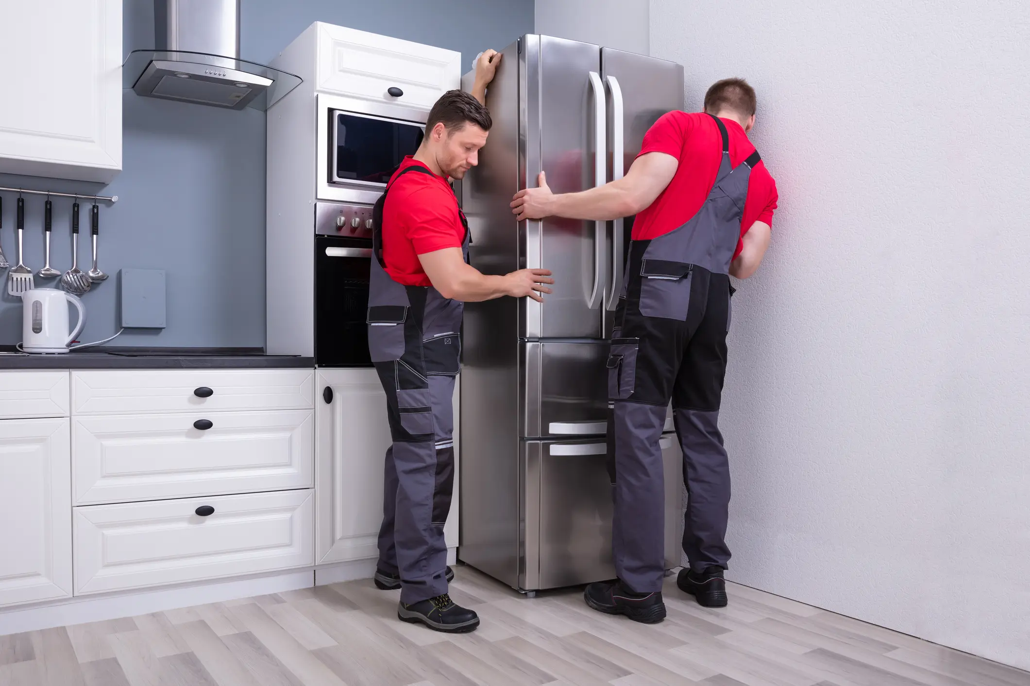 Two technicians installing stainless steel refrigerator in kitchen