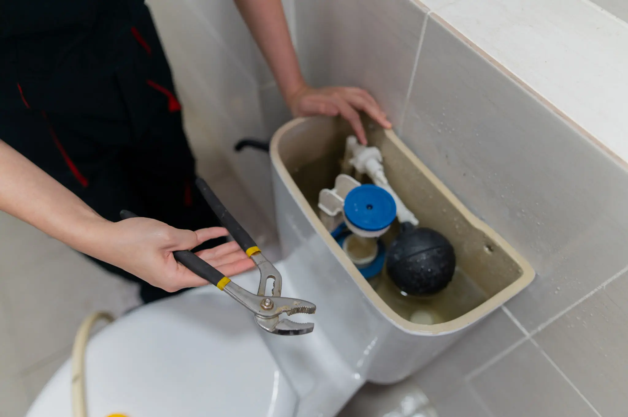 Plumber repairing toilet tank with pliers