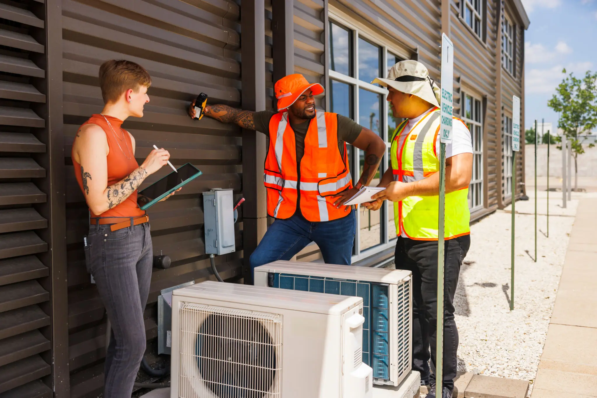 Workers inspecting outdoor HVAC unit beside building
