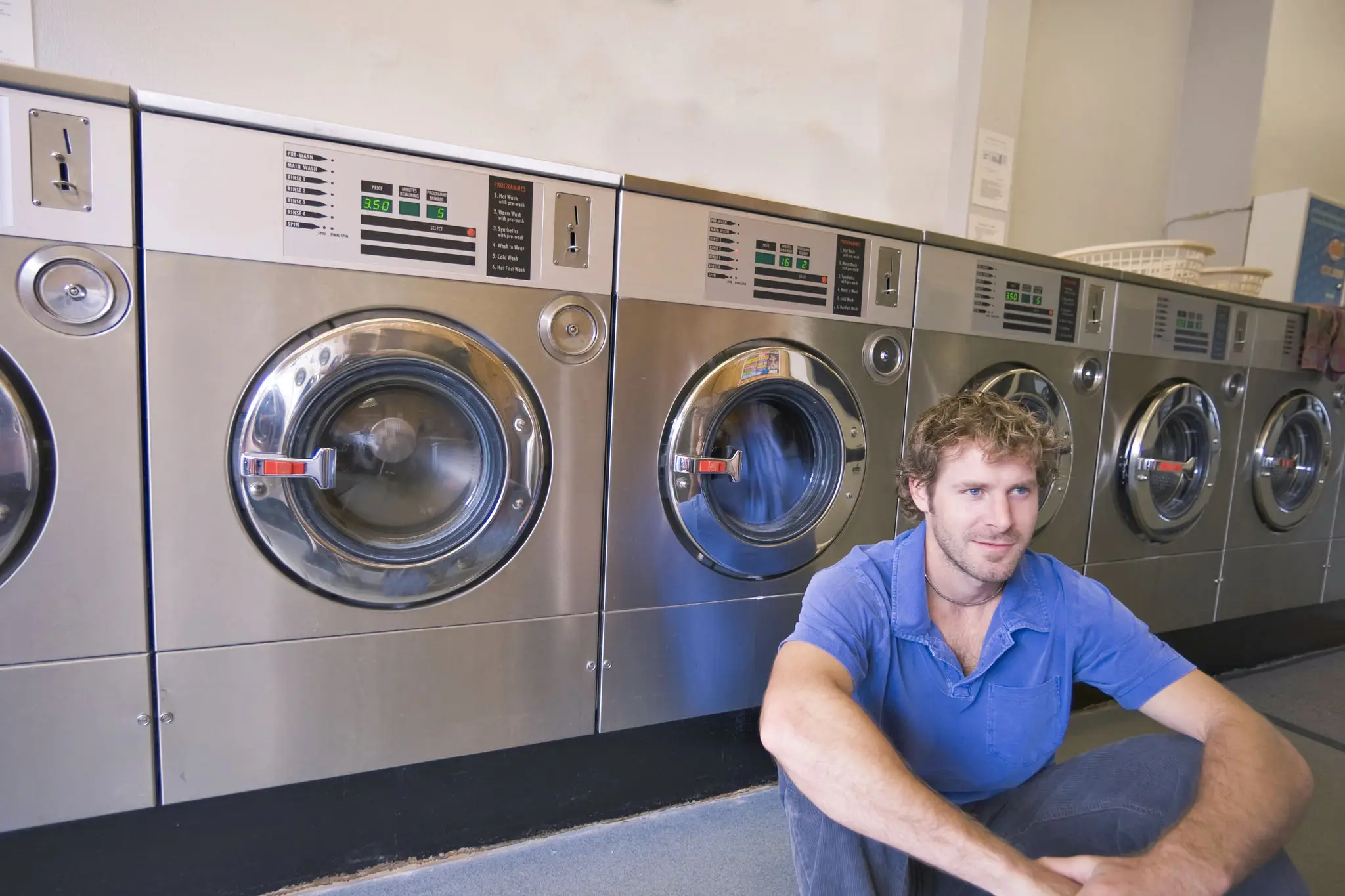 Man sitting in laundromat beside washing machines