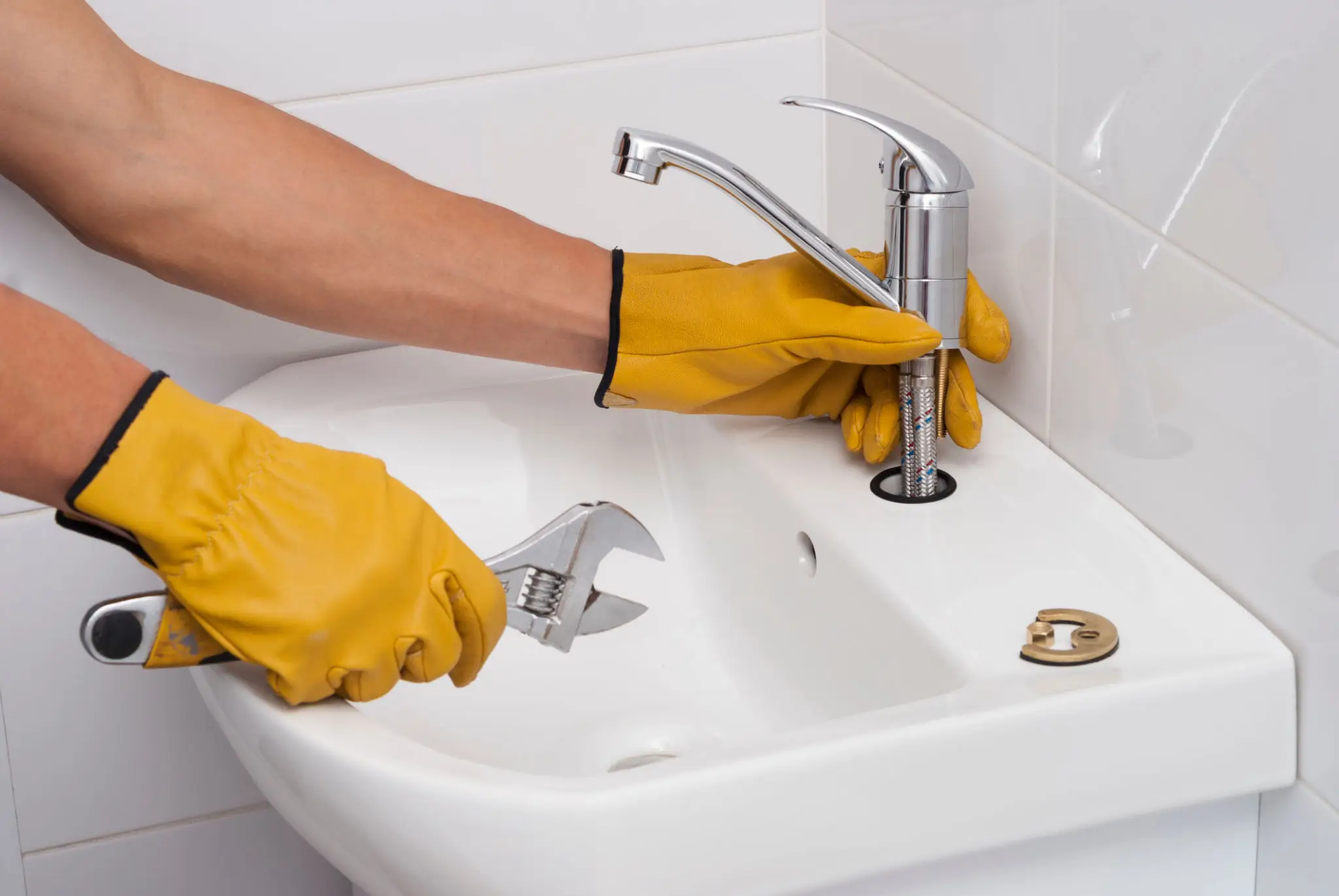 Gloved hands repairing sink faucet with wrench