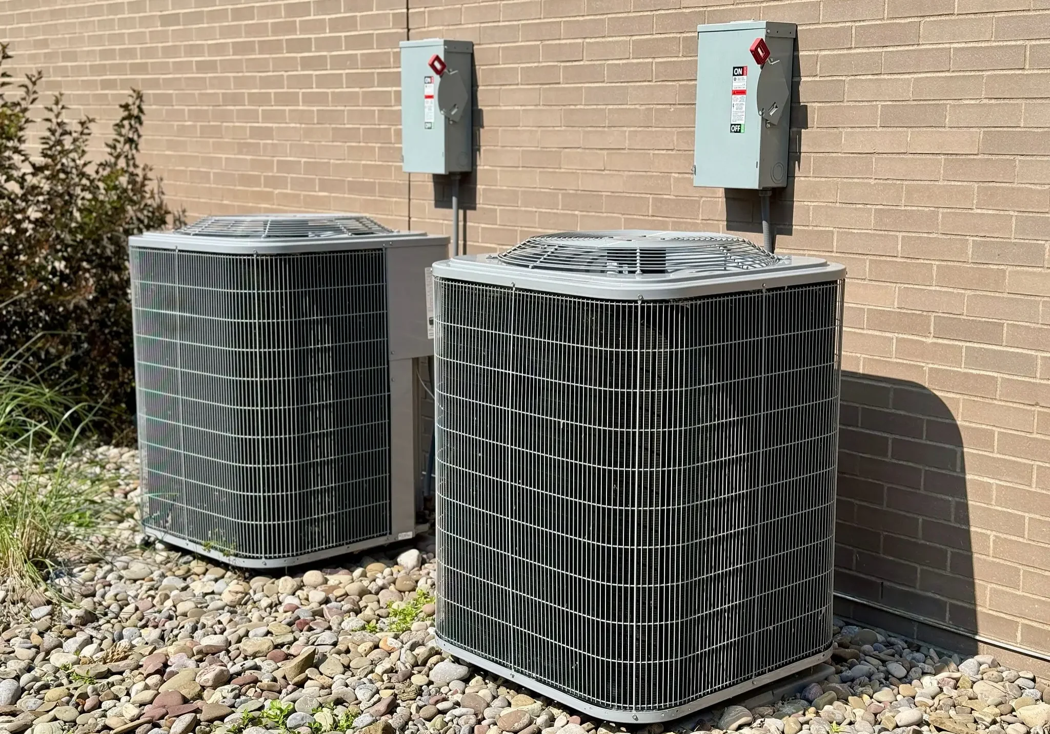 Two outdoor air conditioning units beside brick wall
