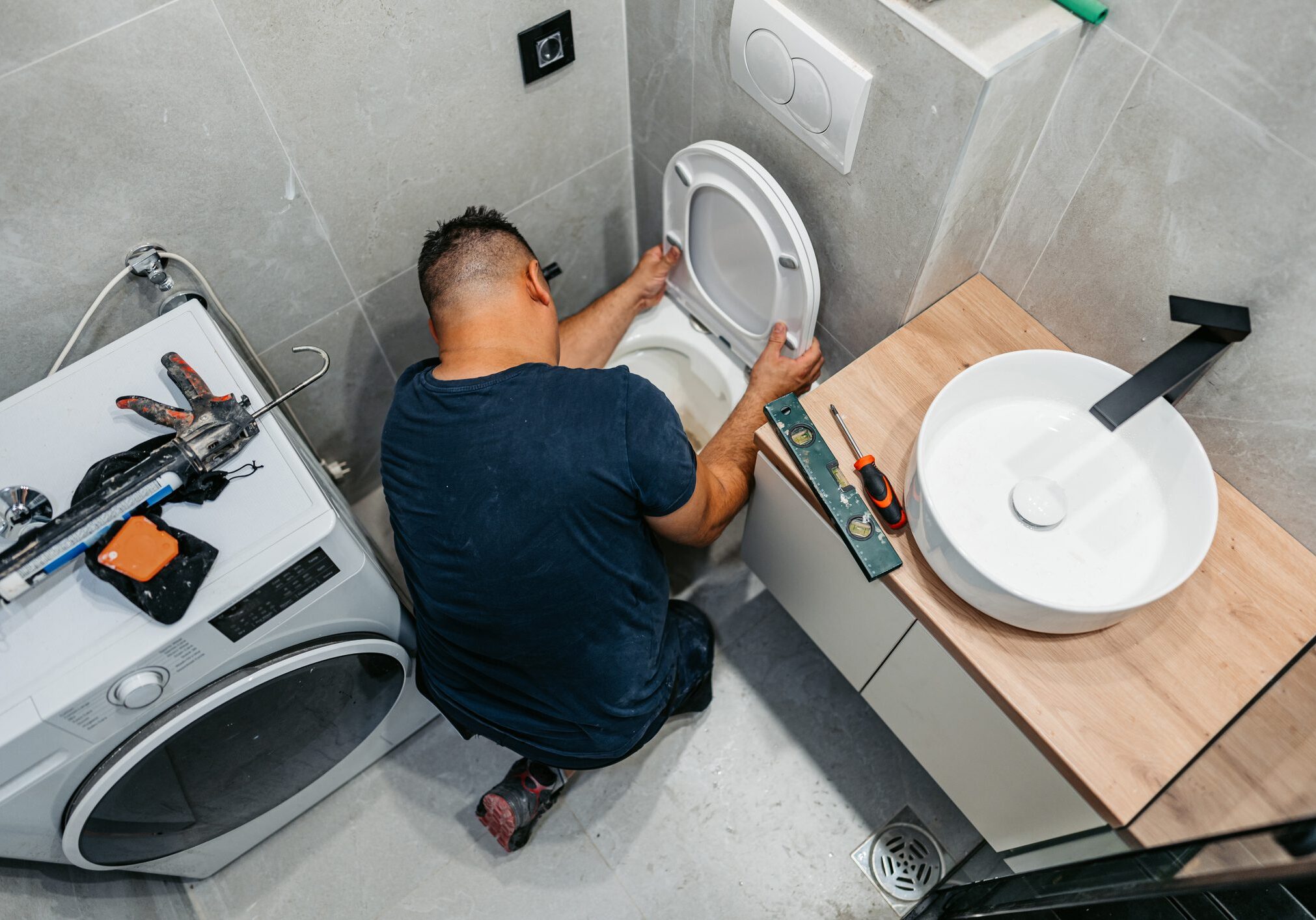 Plumber repairing toilet in compact modern bathroom